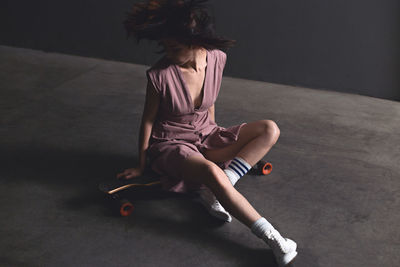 Woman sitting on skateboard against wall 