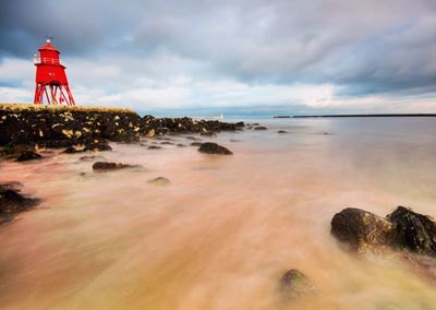 Lighthouse by sea against sky during sunset