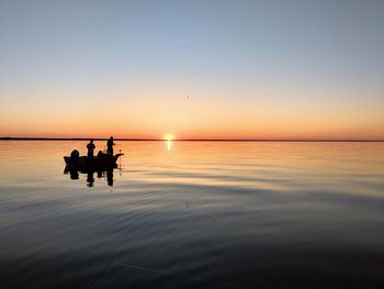 Silhouette people on sea against sky during sunset