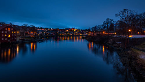 Illuminated city by river against sky at night