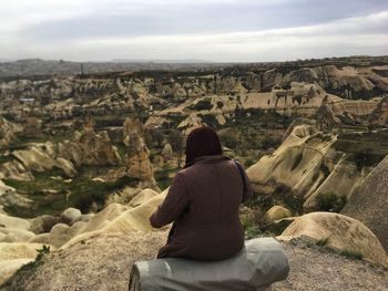 Rear view of woman sitting on rock against sky