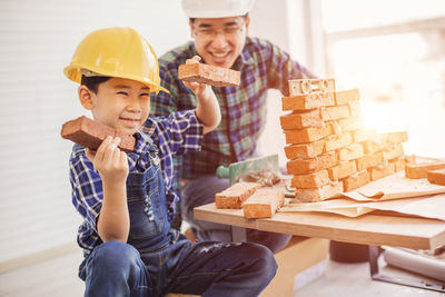 Cute smiling son holding bricks by father at construction site