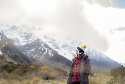 Woman wearing warm clothing while standing against snowcapped mountain