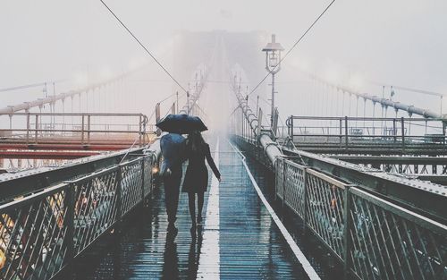 Rear view of couple walking on brooklyn bridge during rainy season