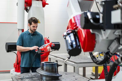 Male engineer operating robotics through control while standing in factory