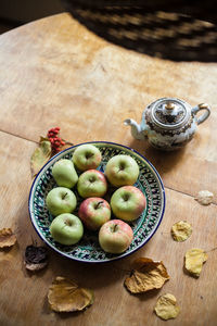 High angle view of apples in plate with dry leaves on wooden table