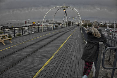 Rear view of woman standing on footbridge against cloudy sky
