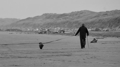 Rear view of man walking on beach against sky