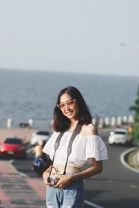 Portrait of smiling young woman standing by sea against sky