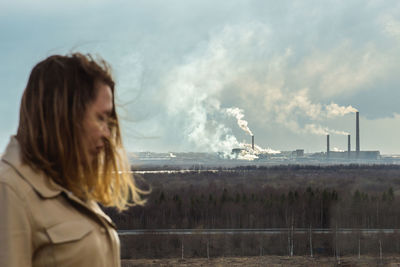 Young woman on smoke emitting from factory against sky