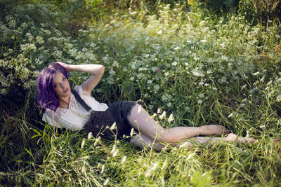 Portrait of a teenage girl with purple hair and an earring in her nose lying in the grass in nature