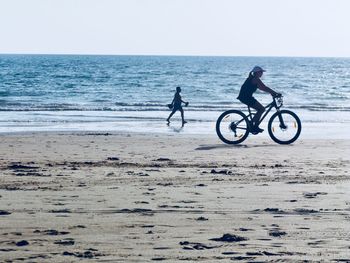 People riding bicycle on beach against clear sky