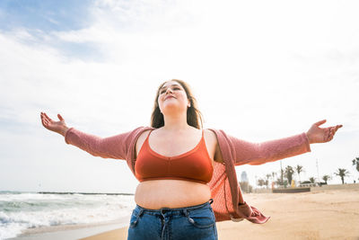 Young woman standing at beach against sky