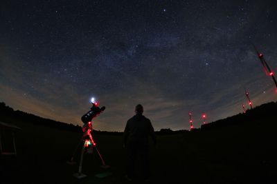 Rear view of man standing by camera against sky at night