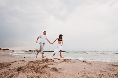 Couple running at beach against sky