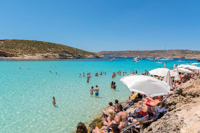 People on beach against clear blue sky