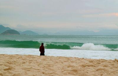 Rear view of man standing on beach against sky