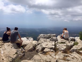 Rear view of people sitting on rocks against sky