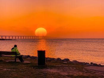 Man looking at sea against orange sky