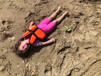 Portrait of boy in life jacket crying while lying at beach