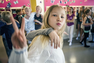 Schoolgirl showing peace sign with friends in corridor