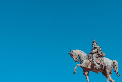 Low angle view of animal sculpture against clear blue sky