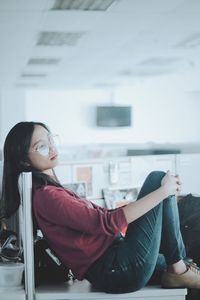 Side view of thoughtful young woman looking away while sitting on table