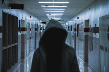 REAR VIEW OF WOMAN WITH ARMS RAISED IN CORRIDOR