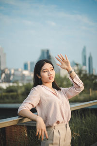 Young woman with arms raised standing in city against sky