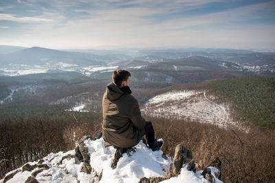 Rear view of man sitting on mountain during winter