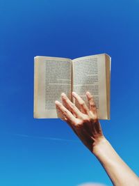 Cropped hand of person holding book against blue background