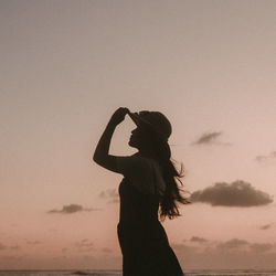 Silhouette woman with arms raised standing against sky during sunset