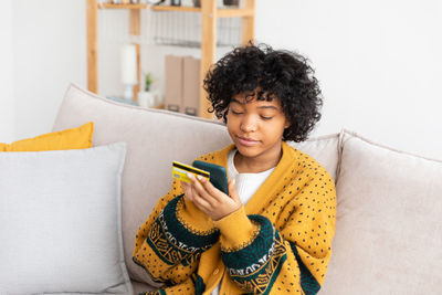 Young woman using mobile phone while sitting on sofa at home