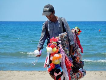 Full length of man holding sunglasses at beach against sky