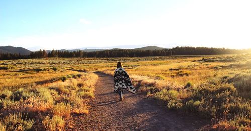 Rear view of woman waking on field against sky during sunset