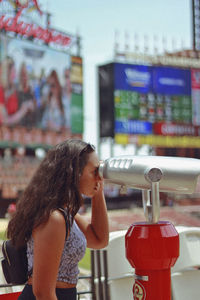 Side view of teenage girl looking through coin-operated binoculars in city