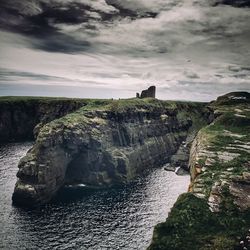 Scenic view of cliff against cloudy sky