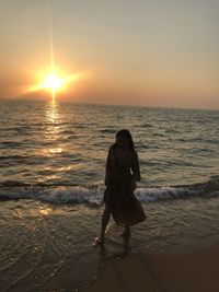 Woman standing on beach against sky during sunset