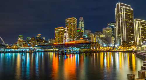 Illuminated city by river at night