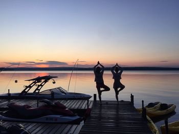 Rear view of women doing yoga pose on pier at sunset