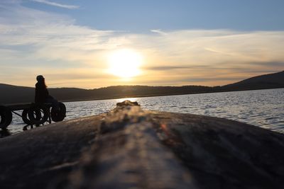 People sitting on shore by sea against sky during sunset