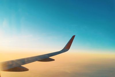 Cropped image of airplane wing against sky during sunset