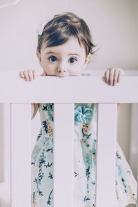 Portrait of cute baby girl standing in crib at home