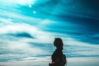 Woman looking away while standing against cloudy sky