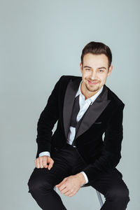 Portrait of happy young man in suit sitting against blue background