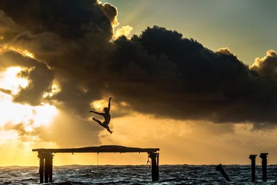 Silhouette woman jumping on built structure over sea