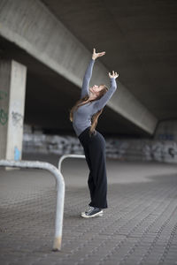 Side view of young woman dancing under bridge