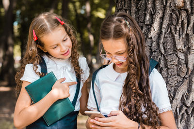 Classmates in school uniform with a book looking at a smartphone on a warm day in the park