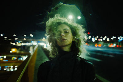Young woman standing against illuminated city at night