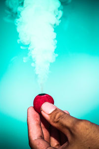 Close-up of hand holding ice cream against blue background